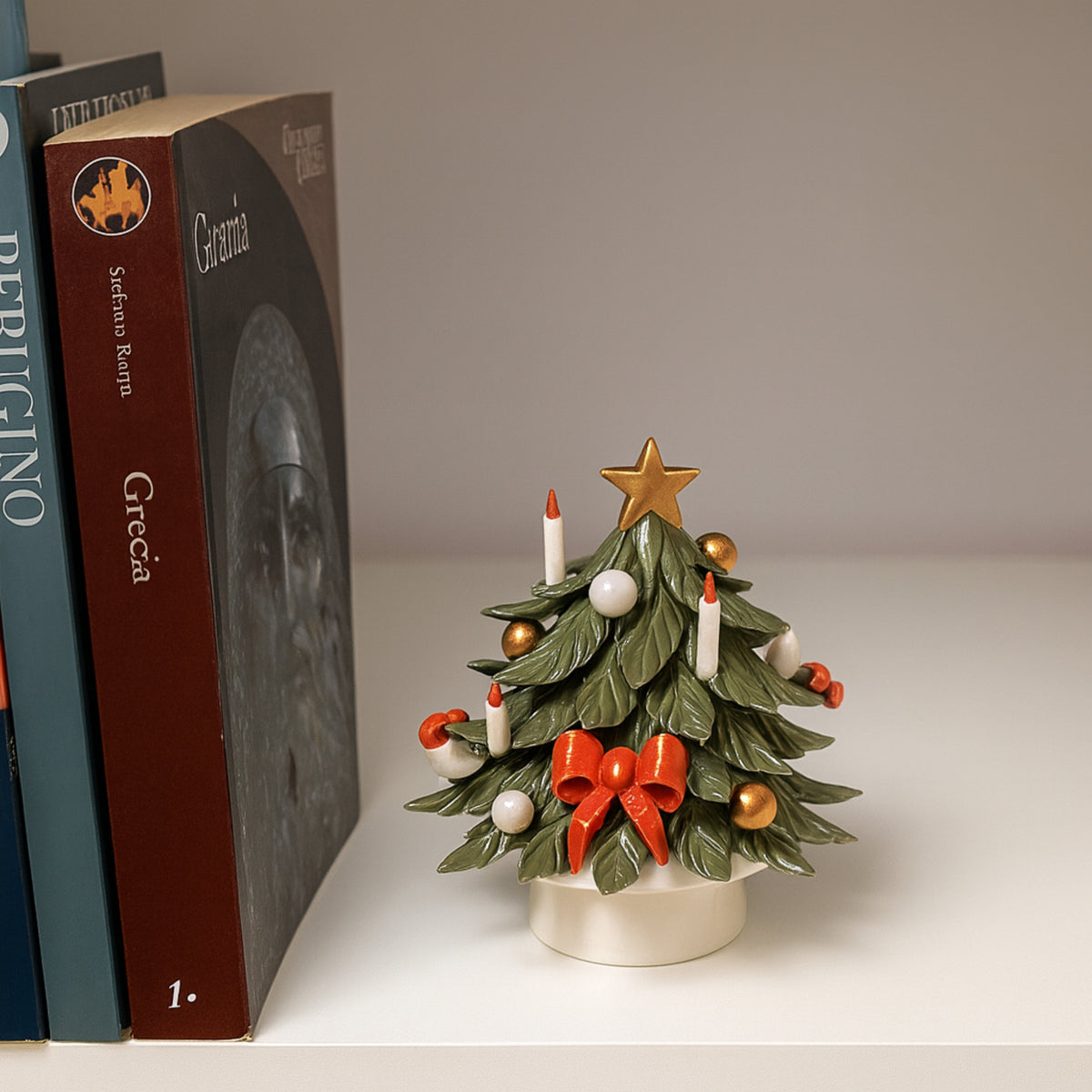 Albero di Natale verde in porcellana con fiocco rosso, palline e stella dorata, accanto ai libri