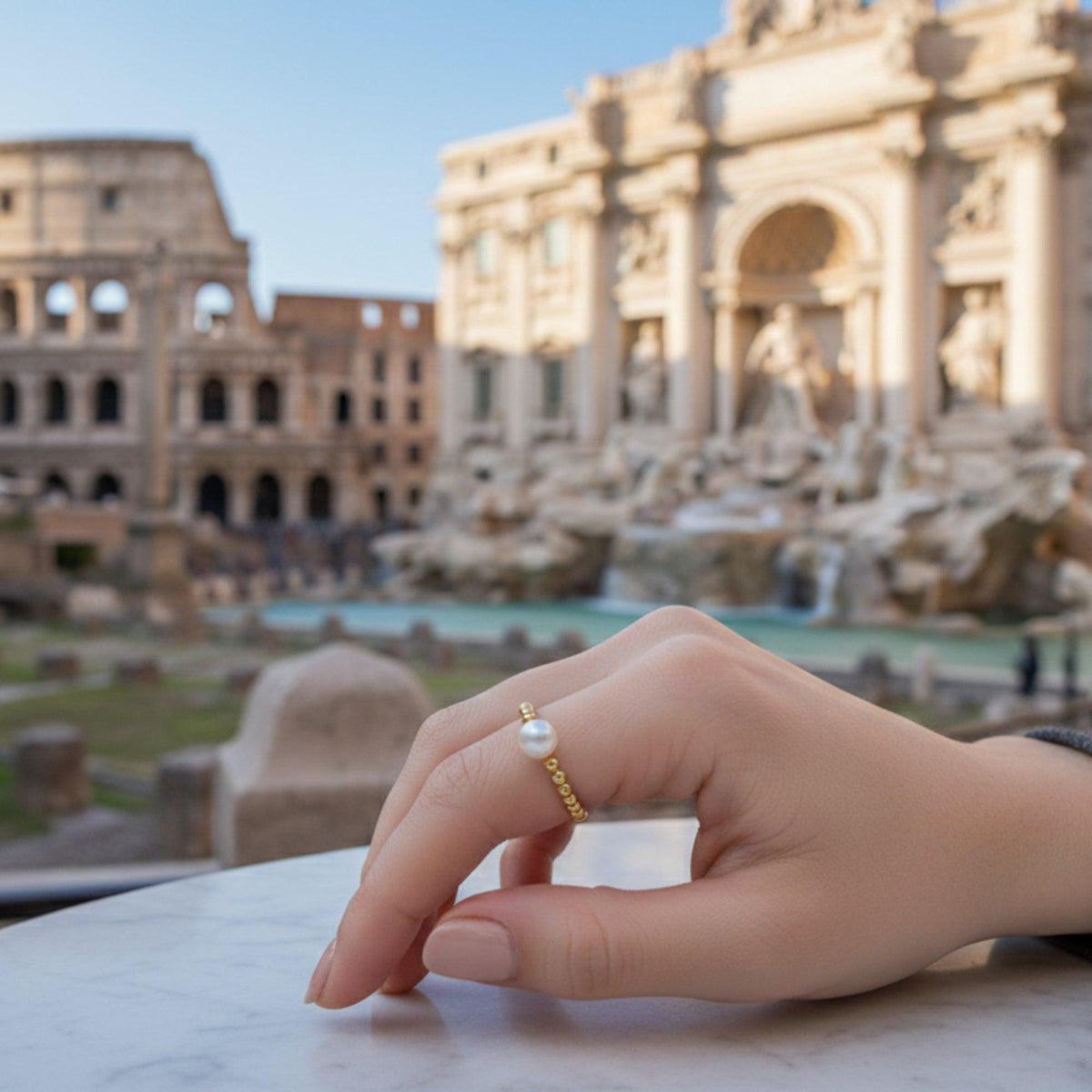 Anello di Pompei con perla bianca, indossato con una fontana e un edificio ad archi sullo sfondo