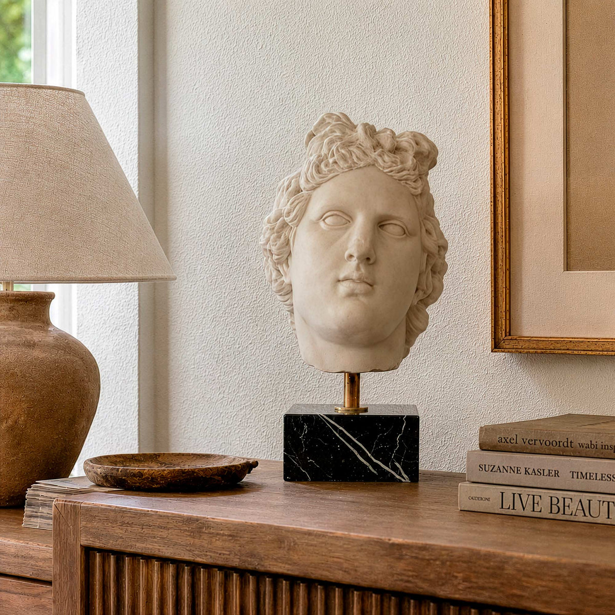 Testa di Artemide in marmo ricomposto su un mobile in legno, accanto a una lampada e a libri