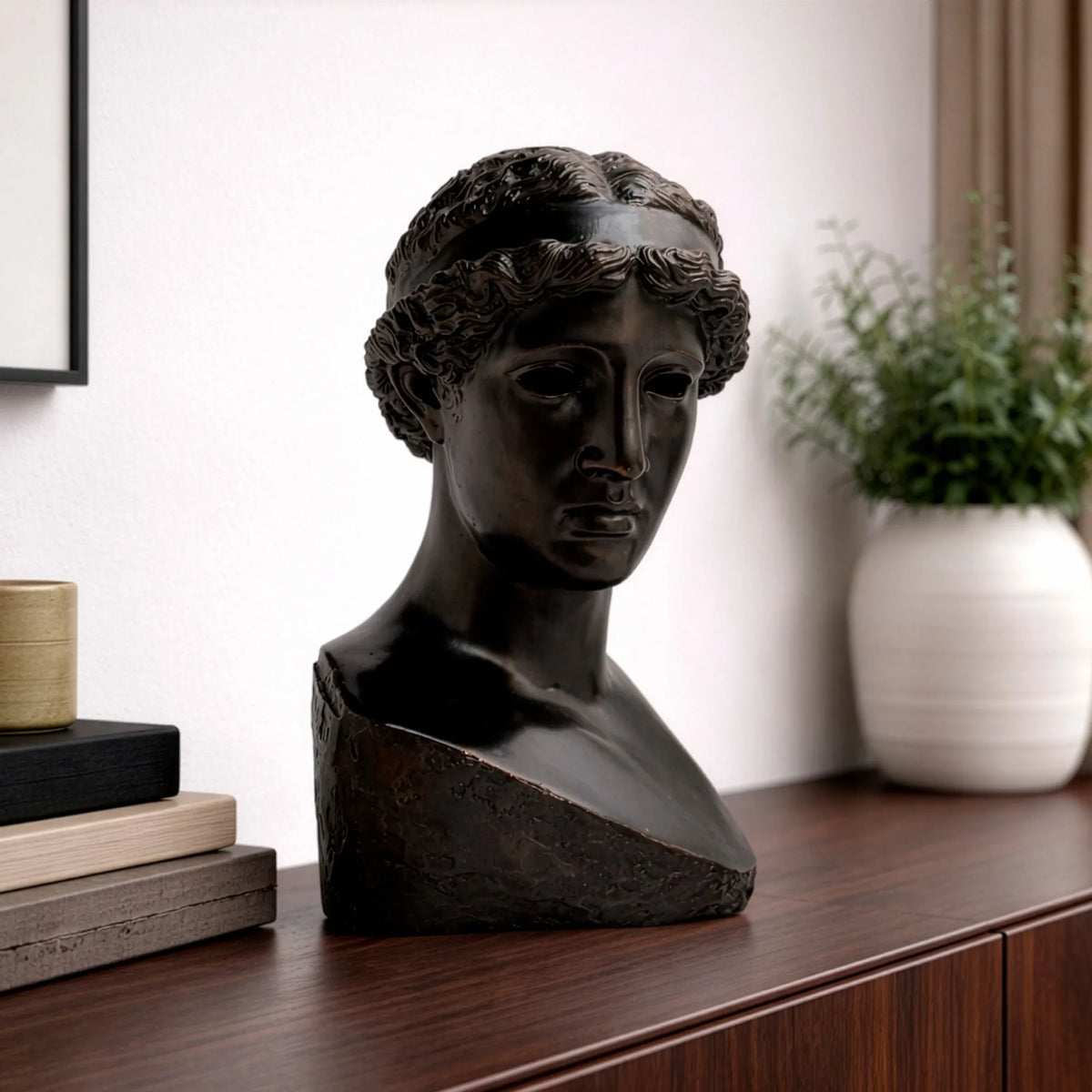 Testa di Atena Lemnia in bronzo nero su un mobile di legno, accanto a libri e a un vaso con pianta.
