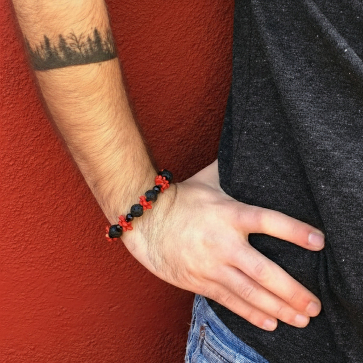 Bracciale in corallo rosso, pietra lavica e onice, indossato al polso davanti a una parete rossa