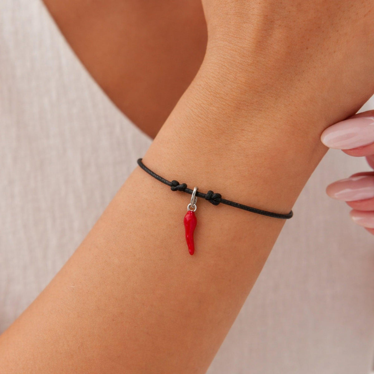 Bracciale con cordoncino nero e piccolo corno in argento smaltato rosso, indossato davanti a una canotta bianca