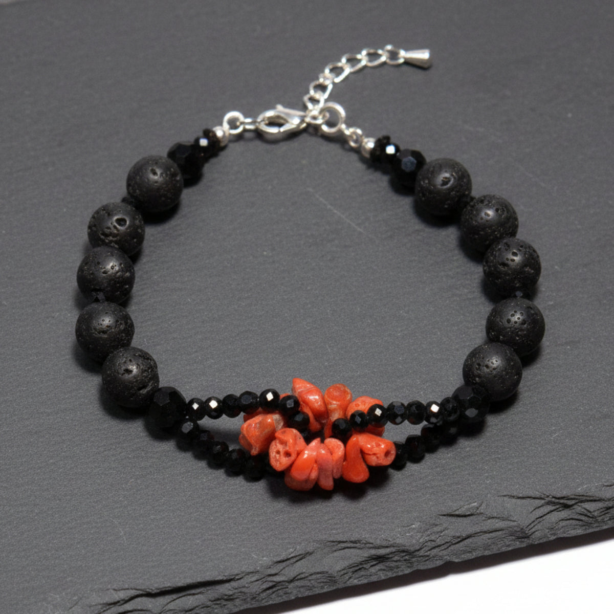 Bracciale con scaglie di corallo rosso, pietra lavica e onice su un piano scuro, con chiusura in argento