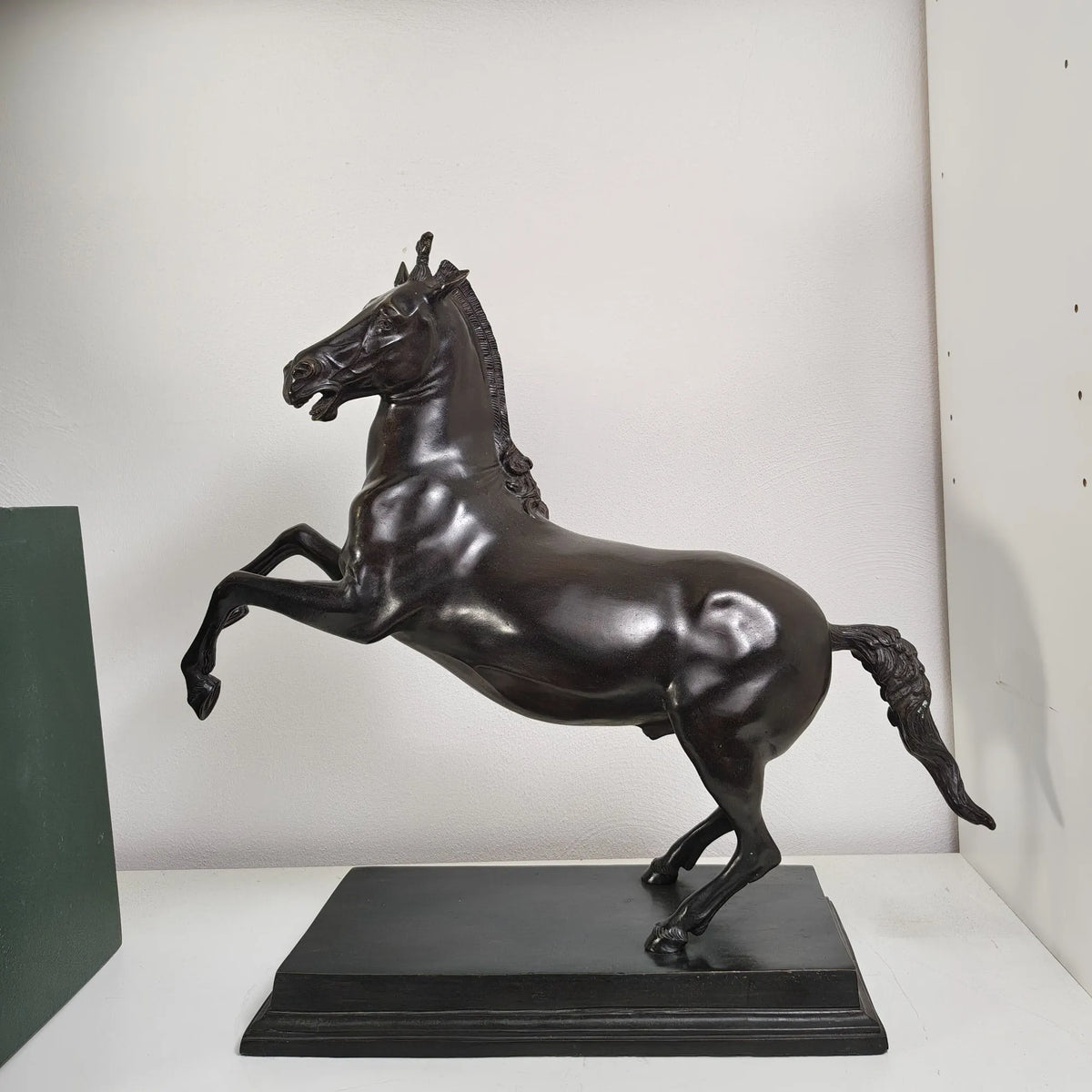 Scultura di Bucefalo in bronzo con testa rivolta a sinistra, esposta su un ripiano bianco accanto a un pannello verde.