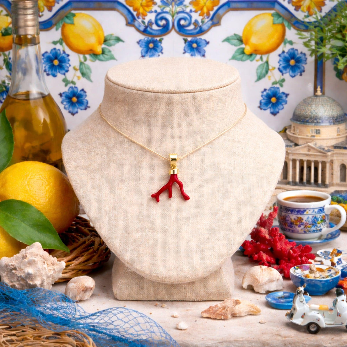 Ciondolo grande a rametti in corallo rosso, su un espositore chiaro tra limoni e ceramiche decorate