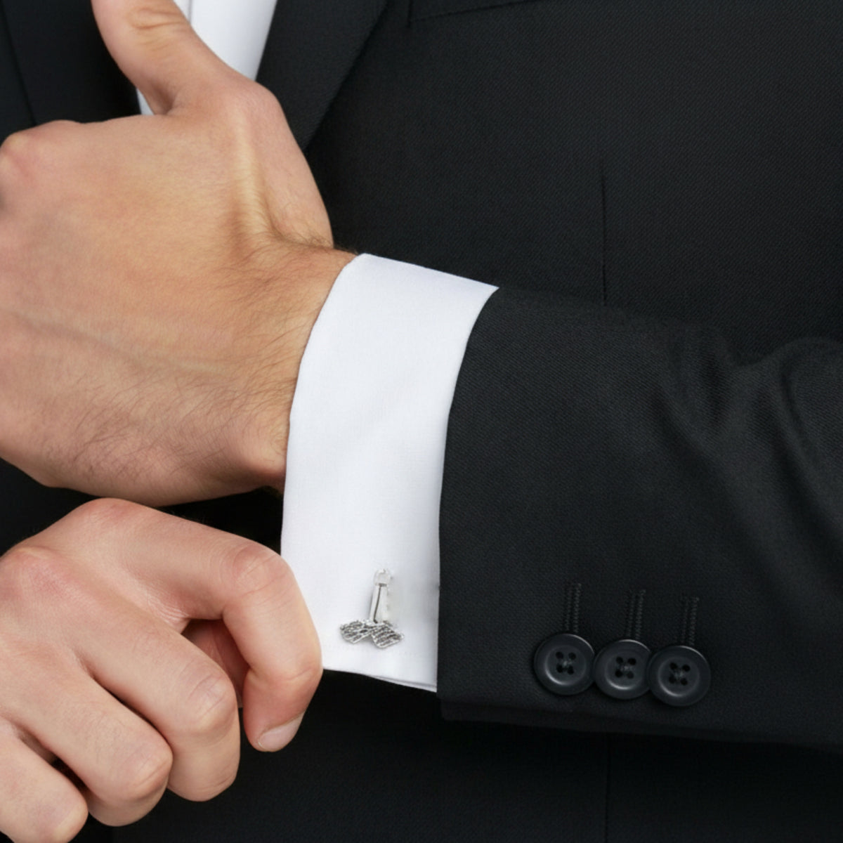 Gemello con fallo alato in argento, indossato sul polsino di una camicia bianca