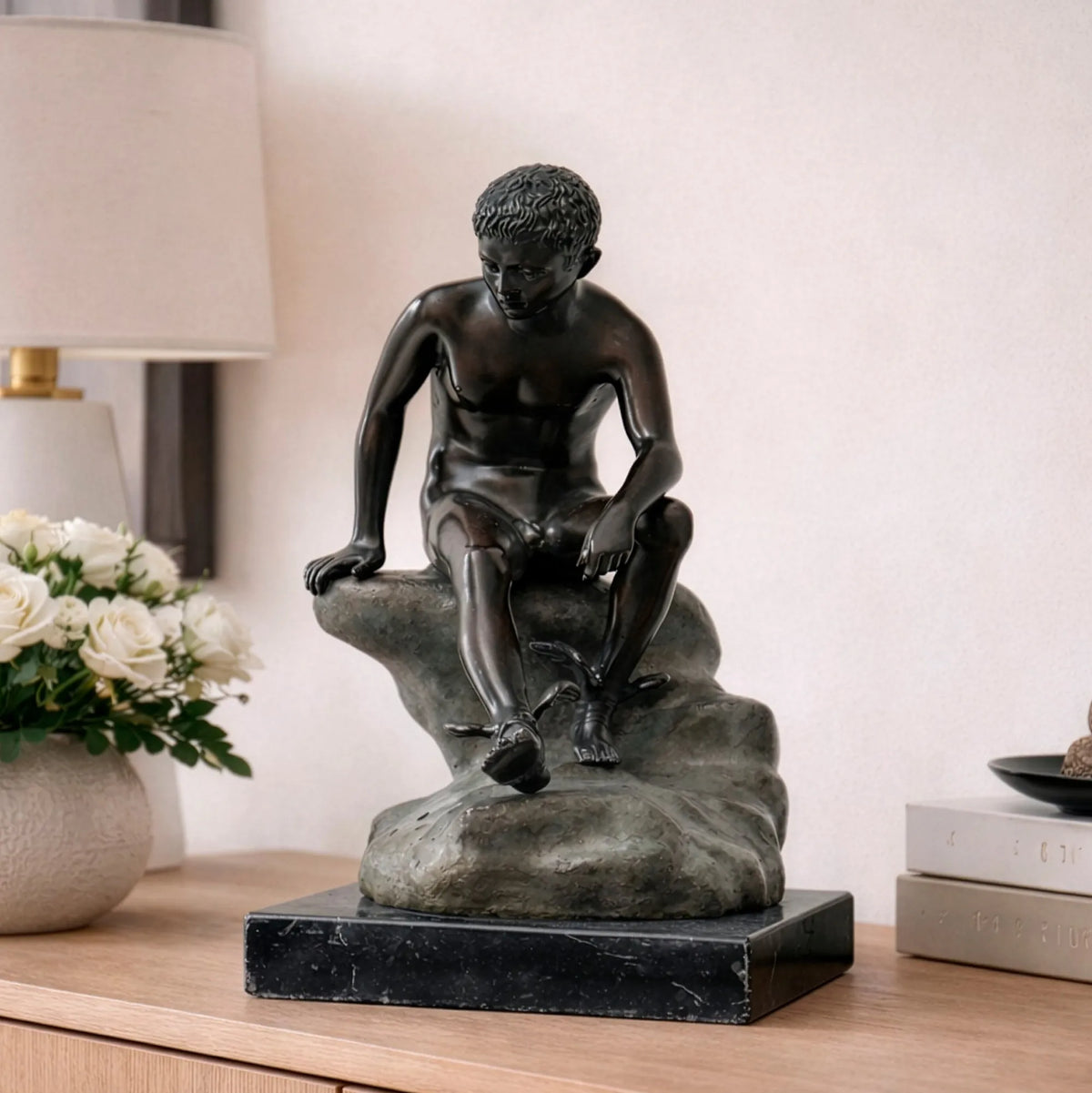 Hermes a riposo in bronzo scuro, statua decorativa seduta su roccia con sandali alati e base in marmo, fotografata in ambiente elegante.
