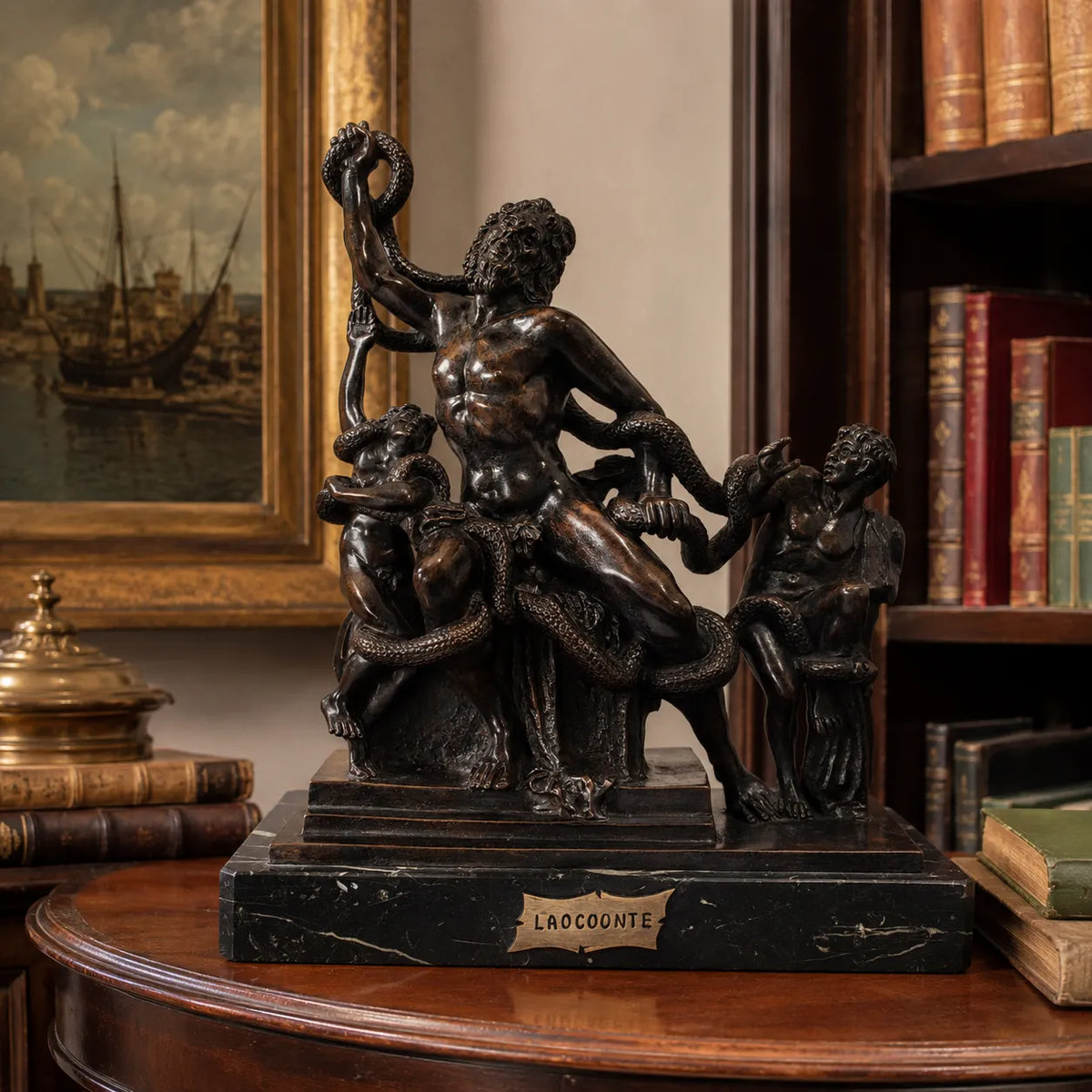 Laocoonte e i suoi figli in bronzo su base in marmo, su un tavolo in legno davanti a una libreria.