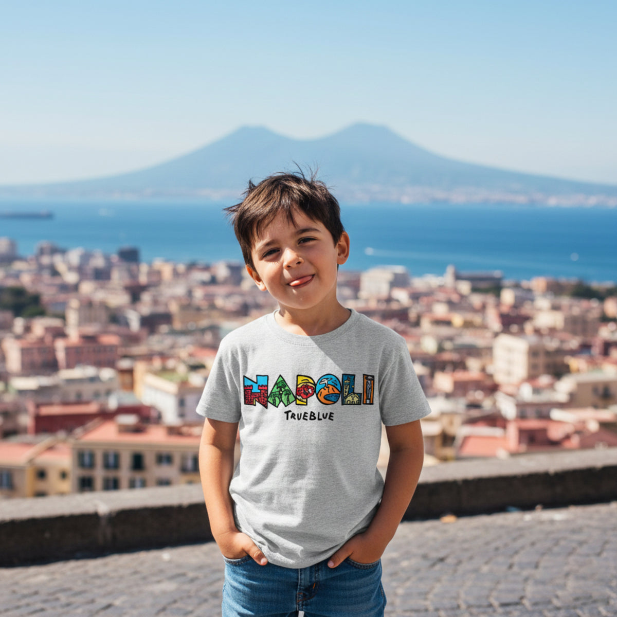 Bambino con maglietta grigia e scritta colorata Napoli TrueBlue, con città e mare sullo sfondo
