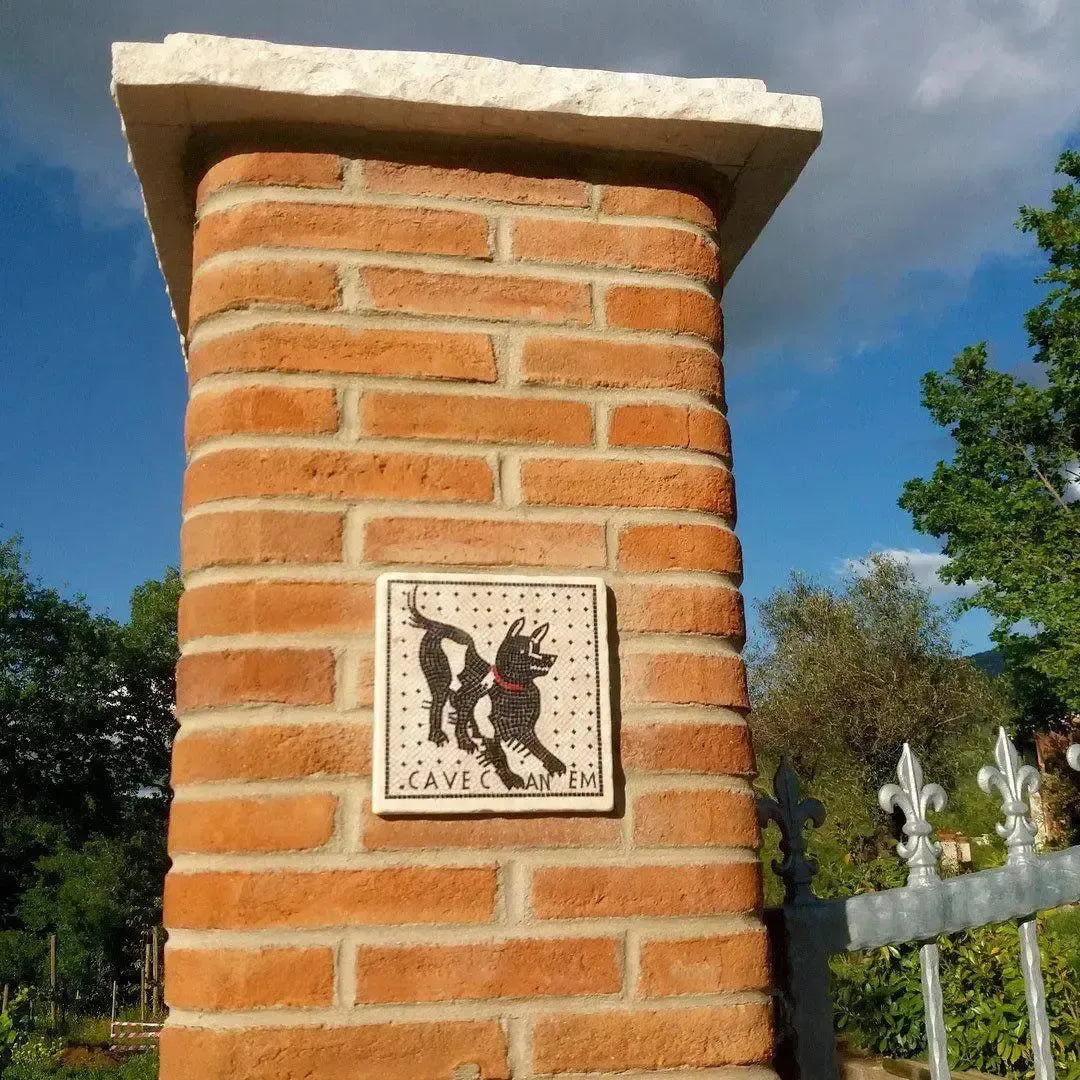 Piastrella Cave Canem montata su un pilastro in mattoni accanto a un cancello