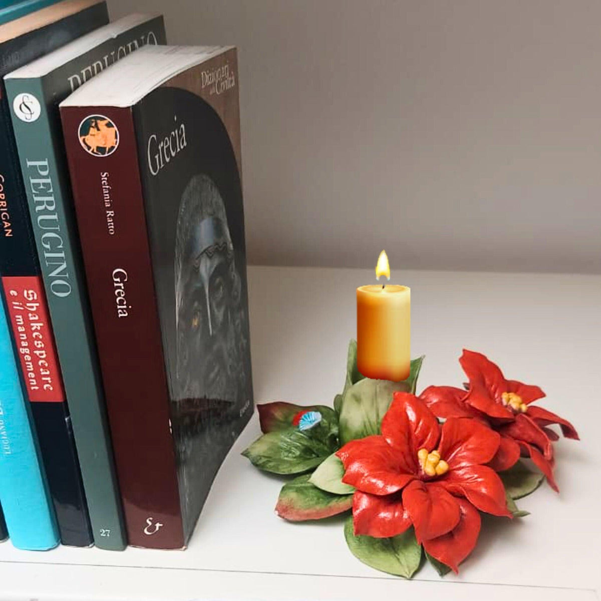 Portacandela in porcellana con stelle di Natale rosse e foglie verdi, con candela accesa accanto ai libri