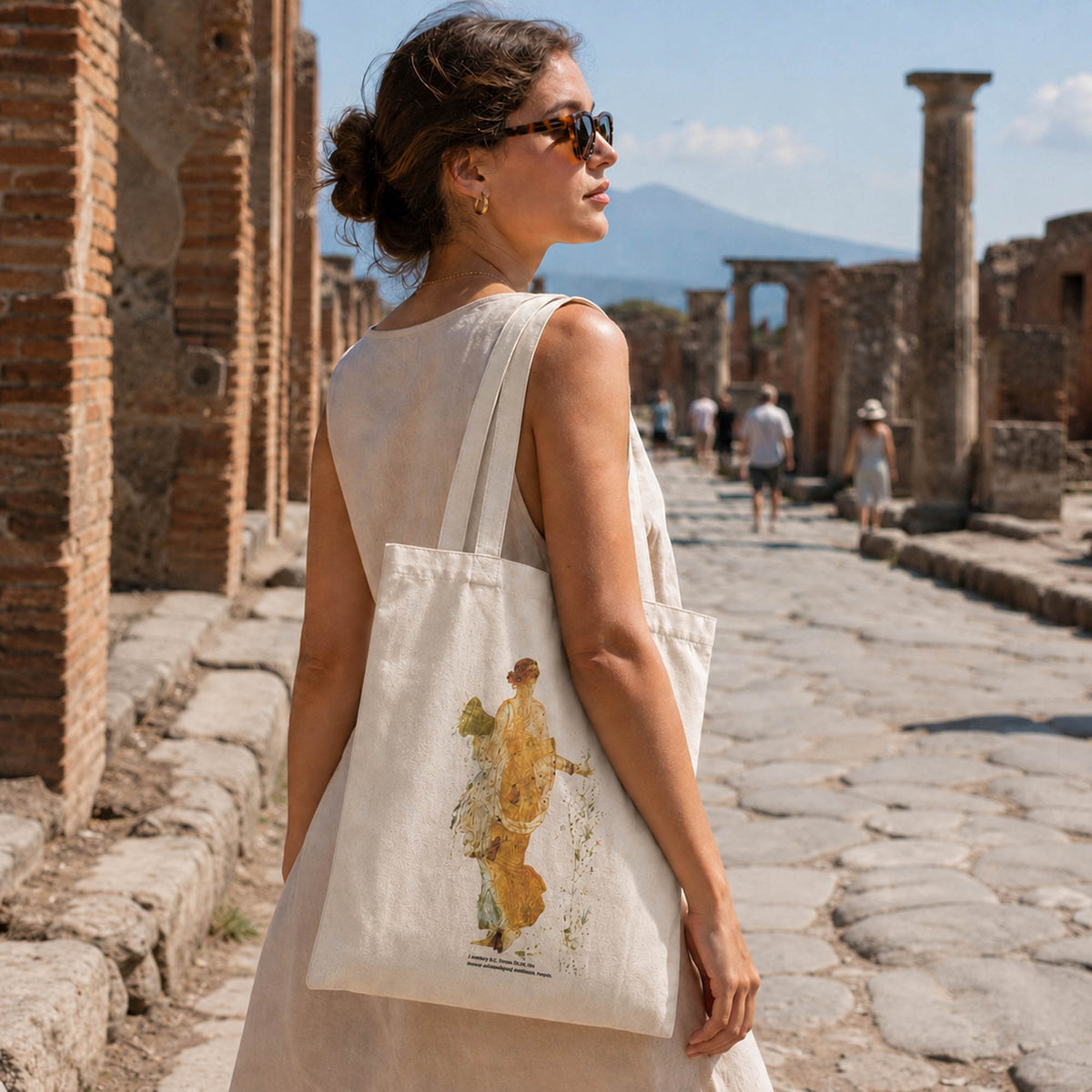 Shopper ecru in cotone con stampa della Flora, portata a spalla tra rovine archeologiche