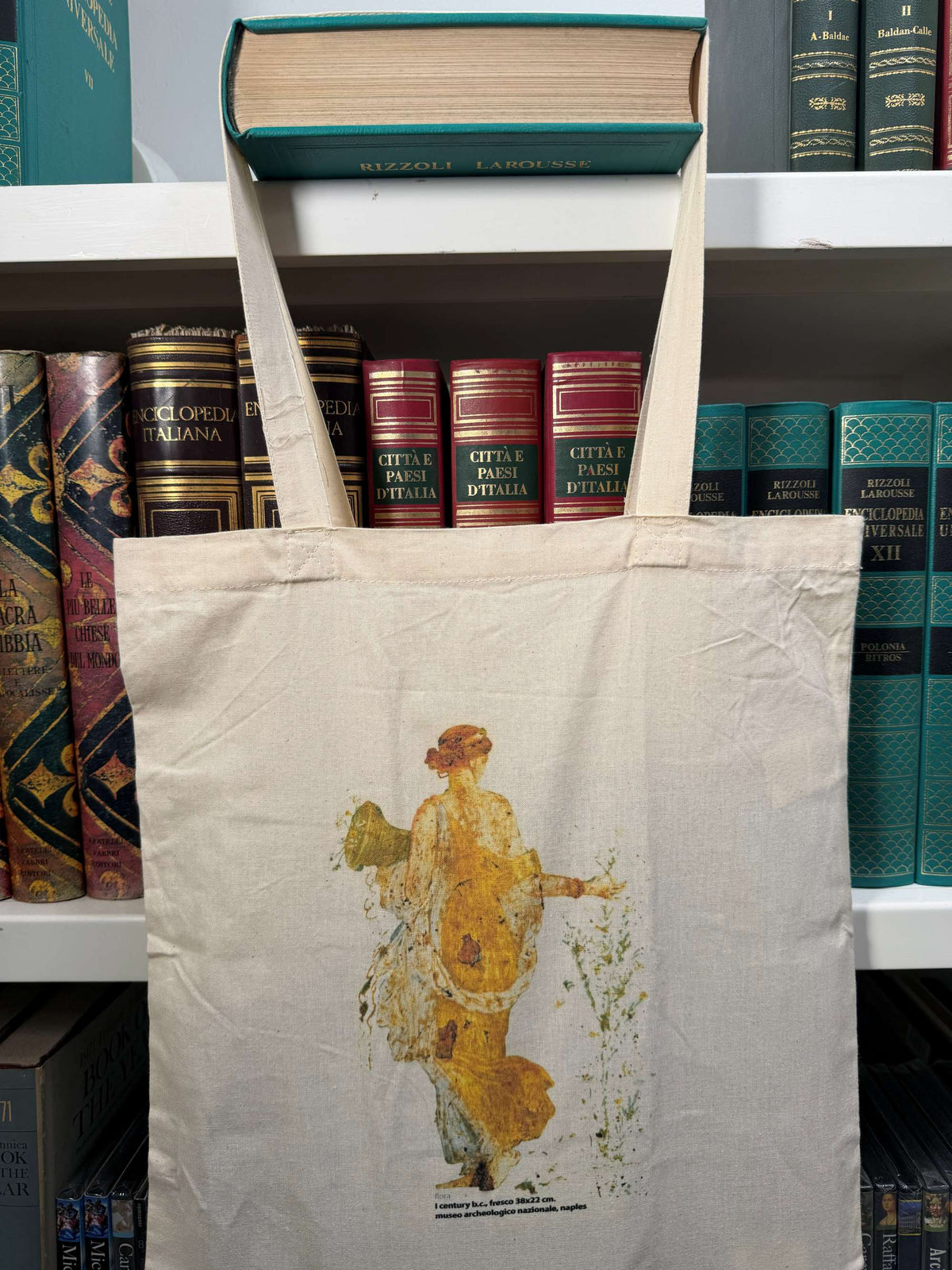 Shopper ecru in cotone con stampa della Flora, appesa davanti a una libreria