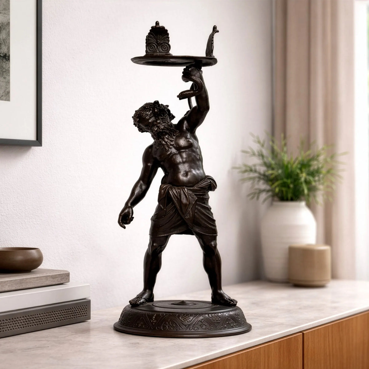 Sileno Pompeiano in bronzo scuro su un mobile, accanto a una pianta in vaso bianco.