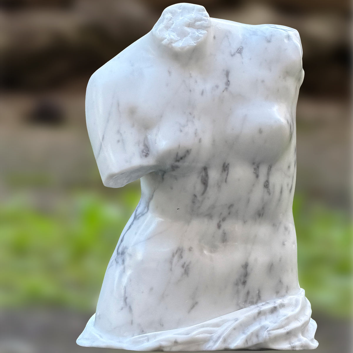 Vista frontale del busto della Venere di Milo in marmo di Carrara in un giardino.