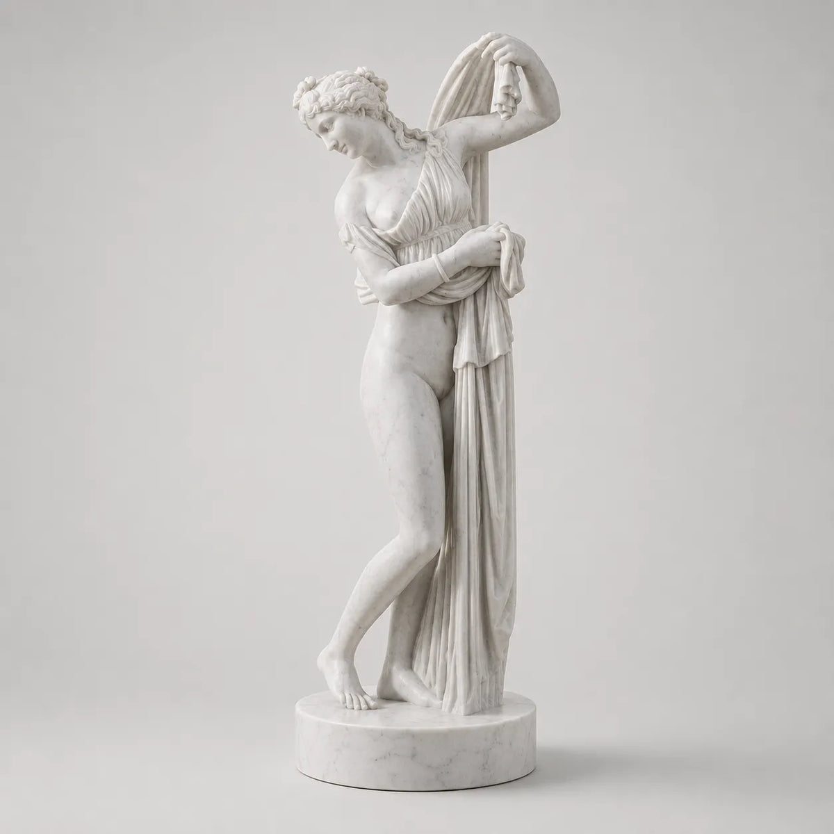 Venere Callipigia in marmo di Carrara, su base circolare e fondo grigio chiaro.