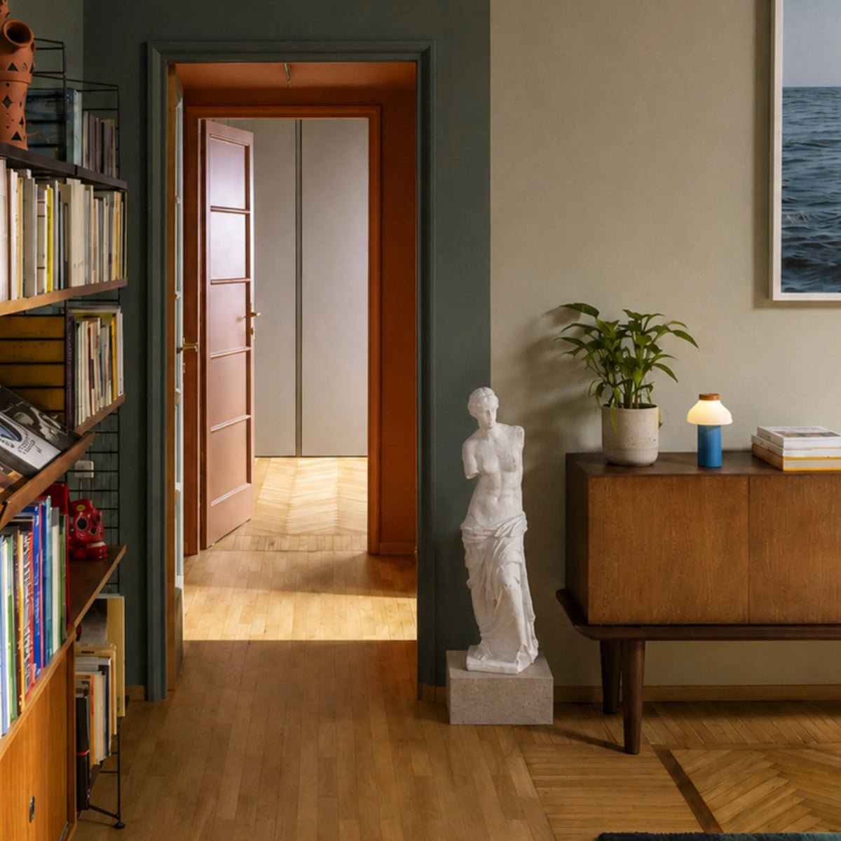 Venere di Milo in marmo di Carrara, su una base chiara in un salotto con libreria.