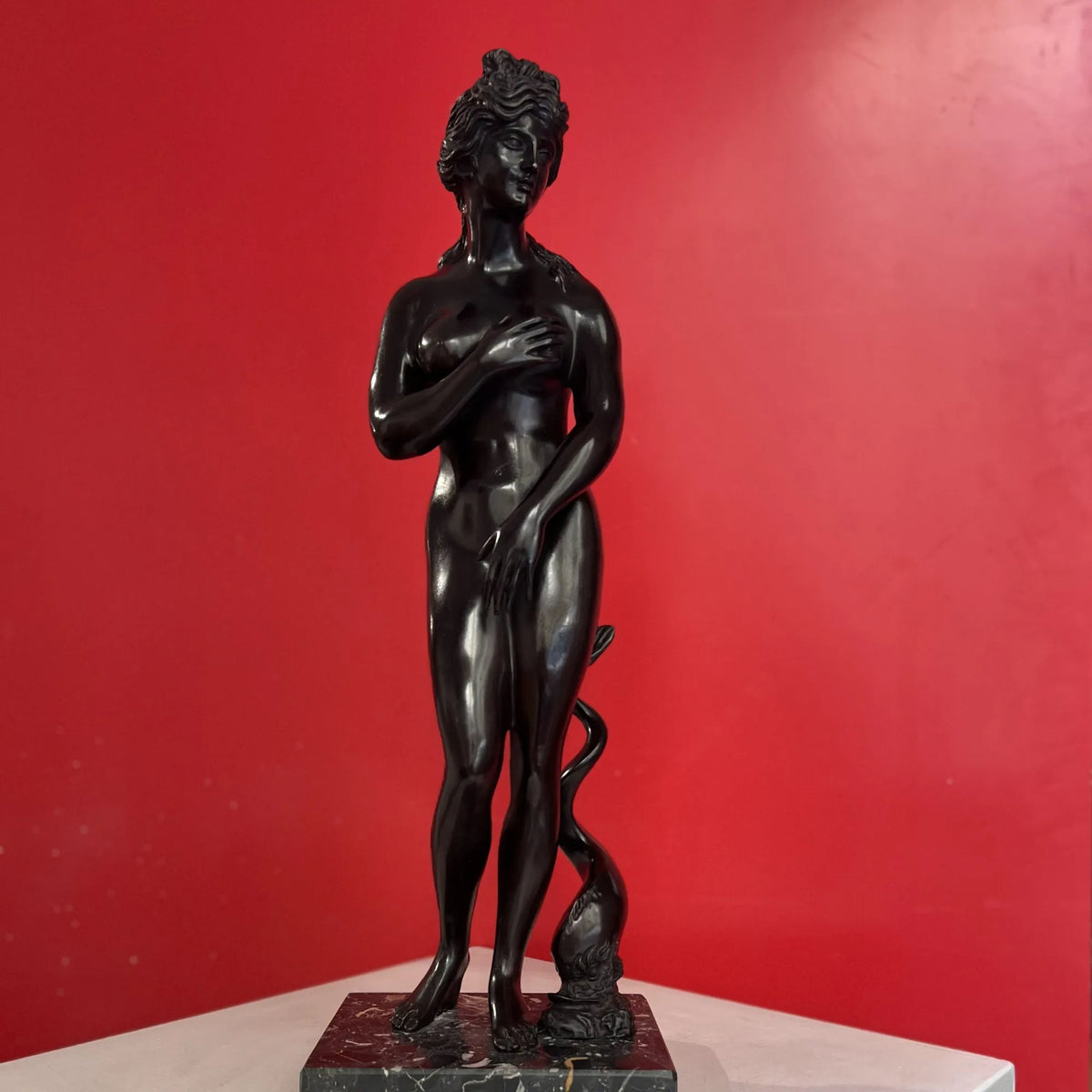 Venere dei Medici in bronzo scuro su base quadrata, vista frontale davanti a una parete rossa.
