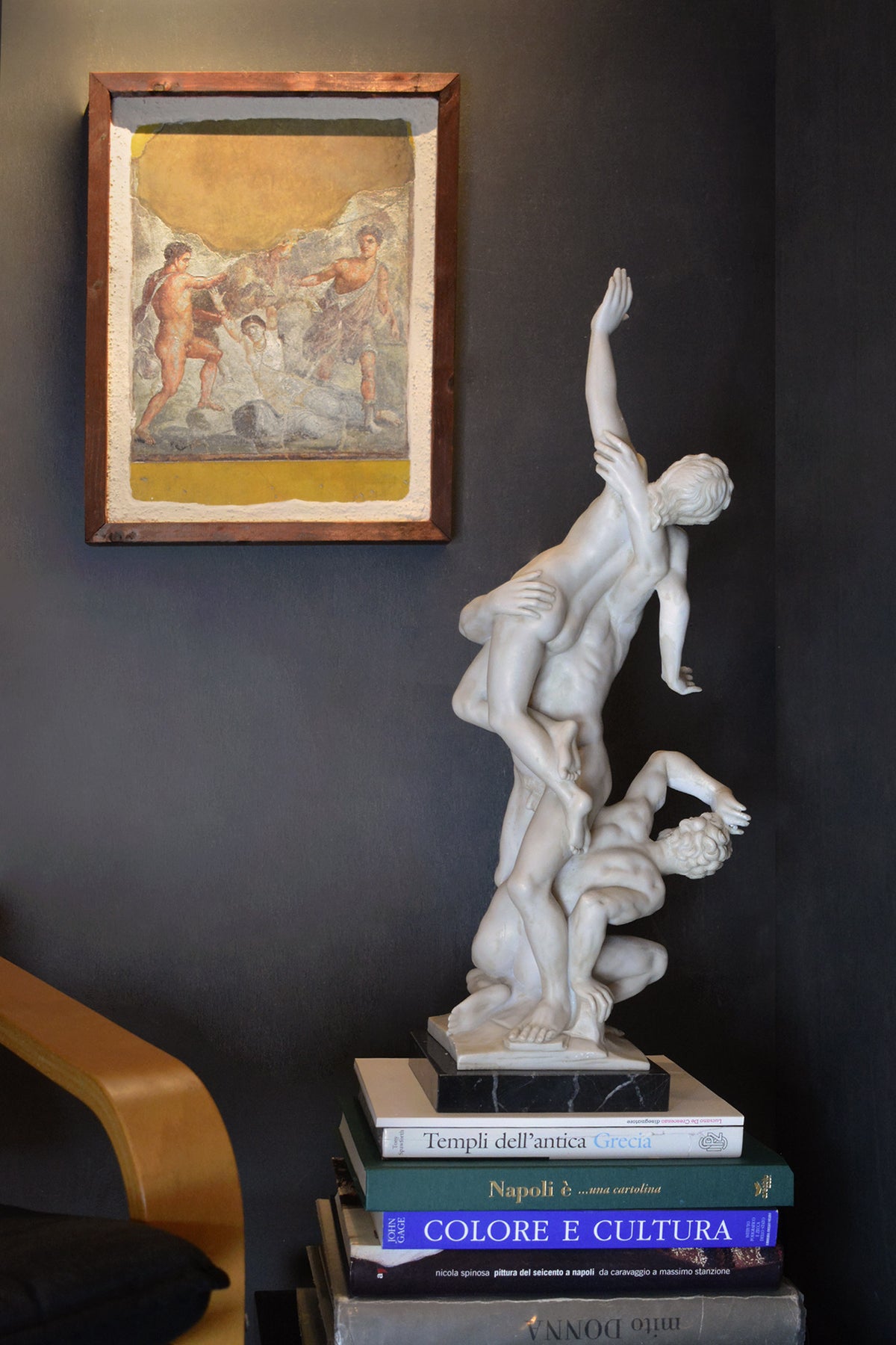 Affresco del castigo di Dirce in cornice su parete scura, accanto a una scultura bianca appoggiata su libri.