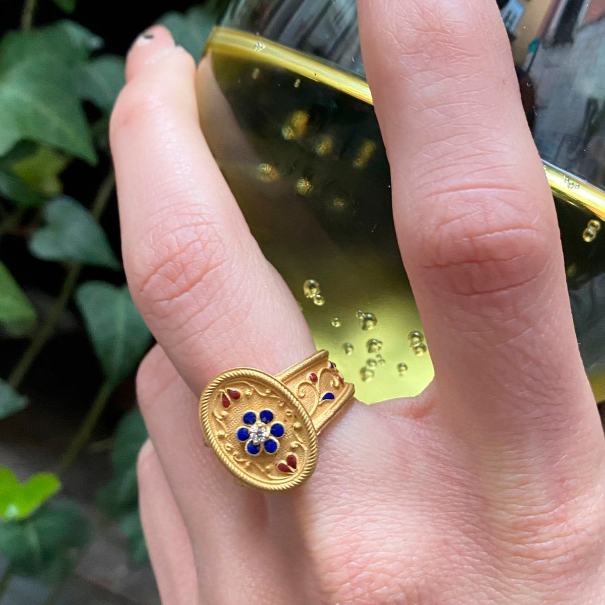 Anello ovale in stile etrusco in oro con smalti blu e rossi e diamante centrale, indossato