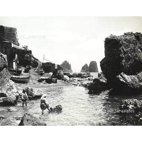 Stampa fotografica Alinari di Marina Piccola a Capri, con due donne nell’acqua, barche sulla riva e Faraglioni sullo sfondo.