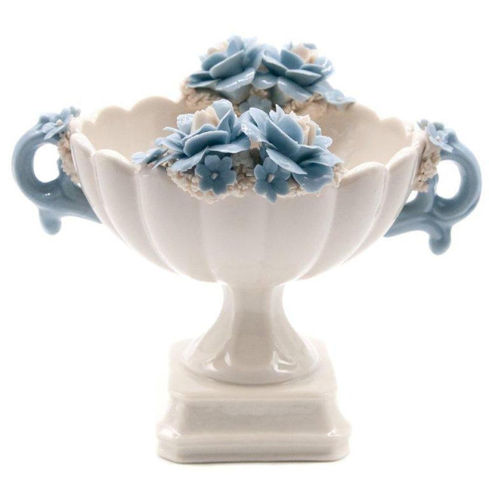 Coppa bianca in porcellana di Capodimonte con fiori e manici azzurri, su fondo bianco.