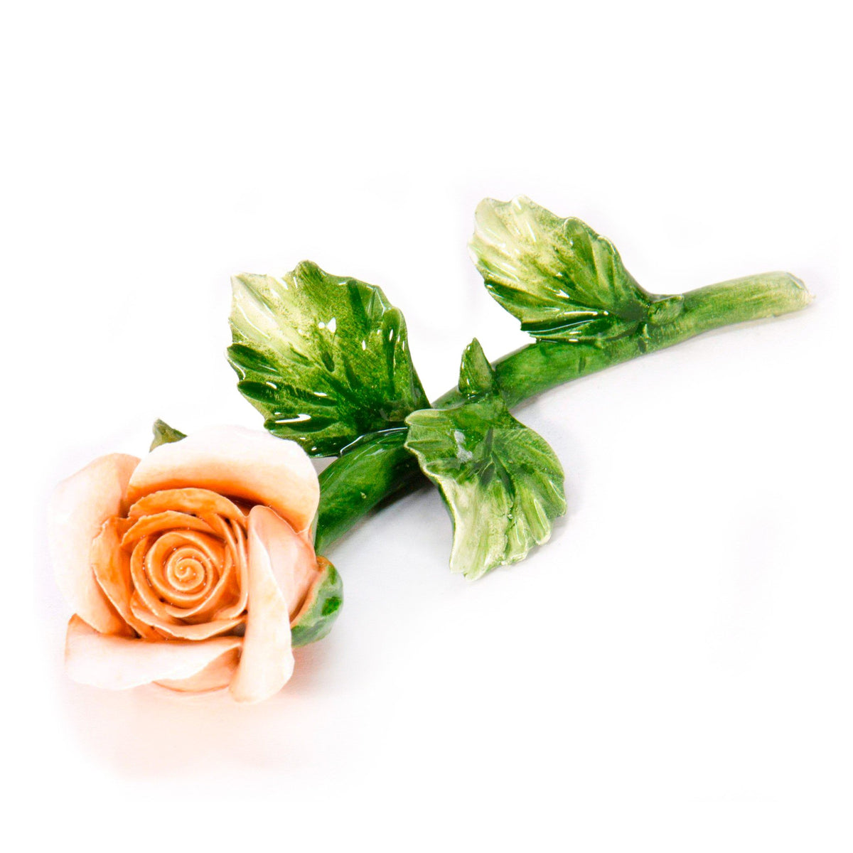 Bocciolo di rosa color pesca in porcellana di Capodimonte, con gambo e foglie verdi su fondo bianco.