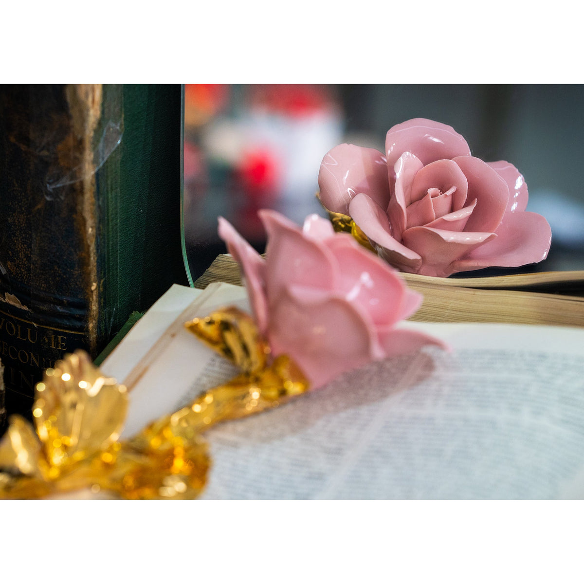 Rosa rosa in porcellana di Capodimonte con gambo dorato, appoggiata su un libro e riflessa nello specchio